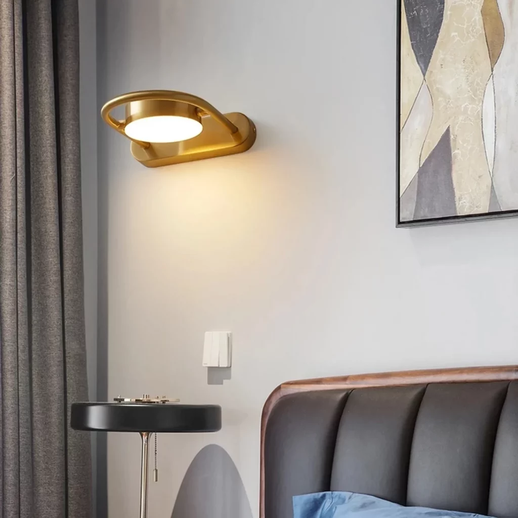 Minimalist Style Gold Round Design Sconce mounted on a modern bedroom wall emitting warm light above a bedside table and upholstered headboard