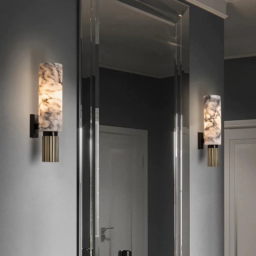 Moonshade Natural Marble Torch Sconce glowing softly on a wall beside a mirror, showing elegant veined marble and warm ambient light.