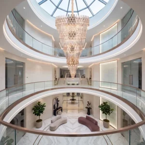 Luxurious multi‑level atrium with circular glass balconies, marble floor, plants, and a cascading crystal chandelier under a skylight.