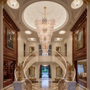 Opulent hotel foyer with a tall crystal chandelier, curved marble staircase, and gilded walls.