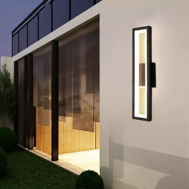 Black Gold Waterproof Outdoor Wall Lamp: Sleek gold rectangular wall sconce illuminating an exterior facade next to large windows.
