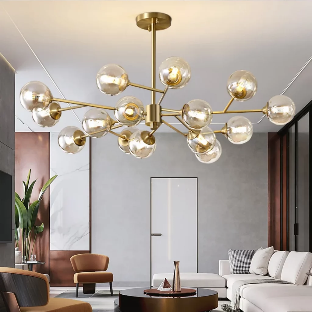 Sputnik Style Arm Chandelier in brushed brass with clear glass globes, illuminating a modern living room with sofa and lounge chairs.