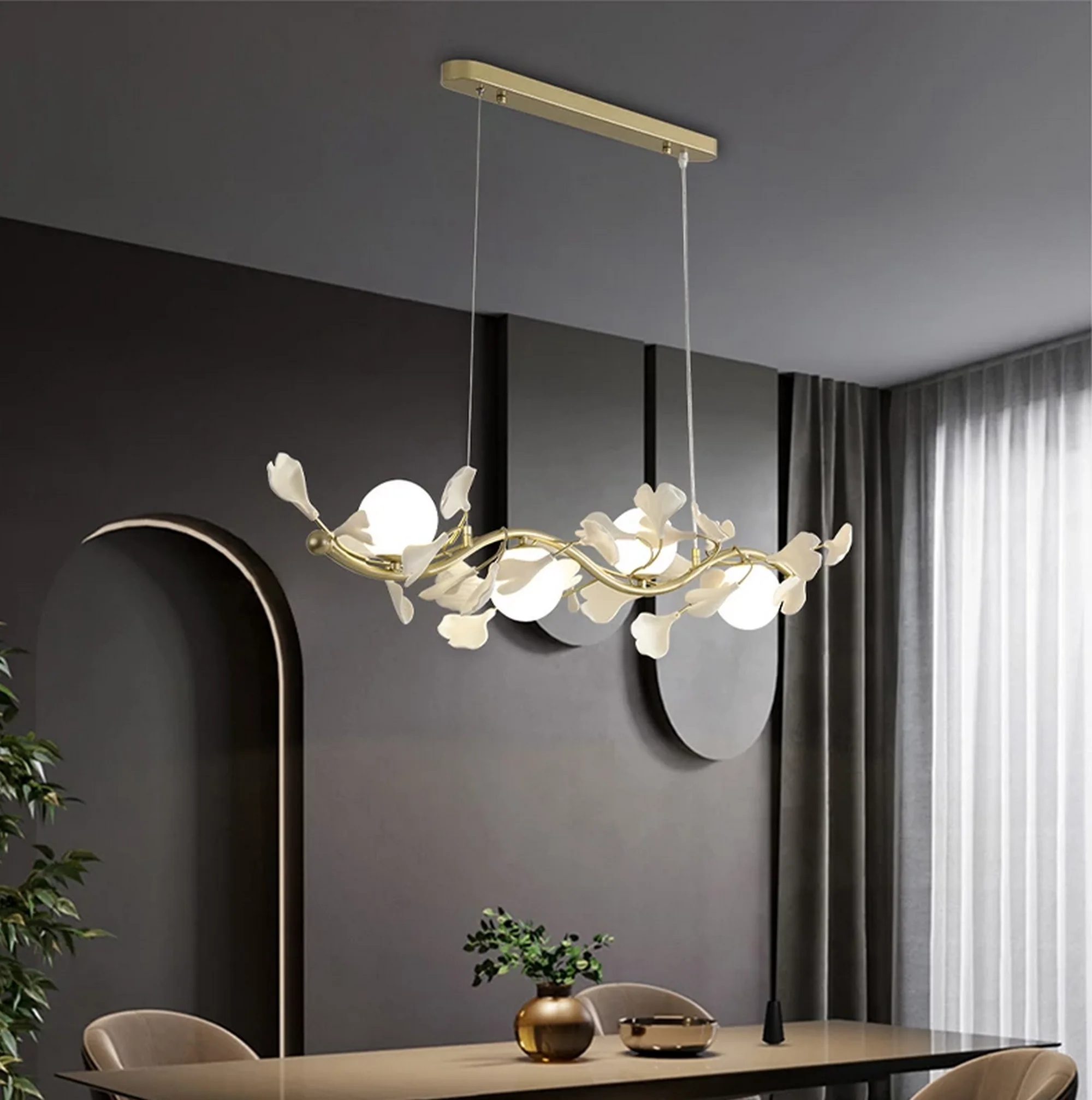 Ginkgo Linear Glass Chandelier featuring a gold wavy branch with white leaf accents and glowing globe bulbs over a dining table.
