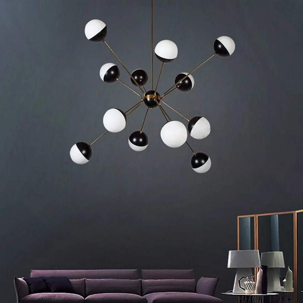 A Rewire Custom Orb Chandelier with striking black and white globes on thin brass arms creates a bold, modern look in a dark room.